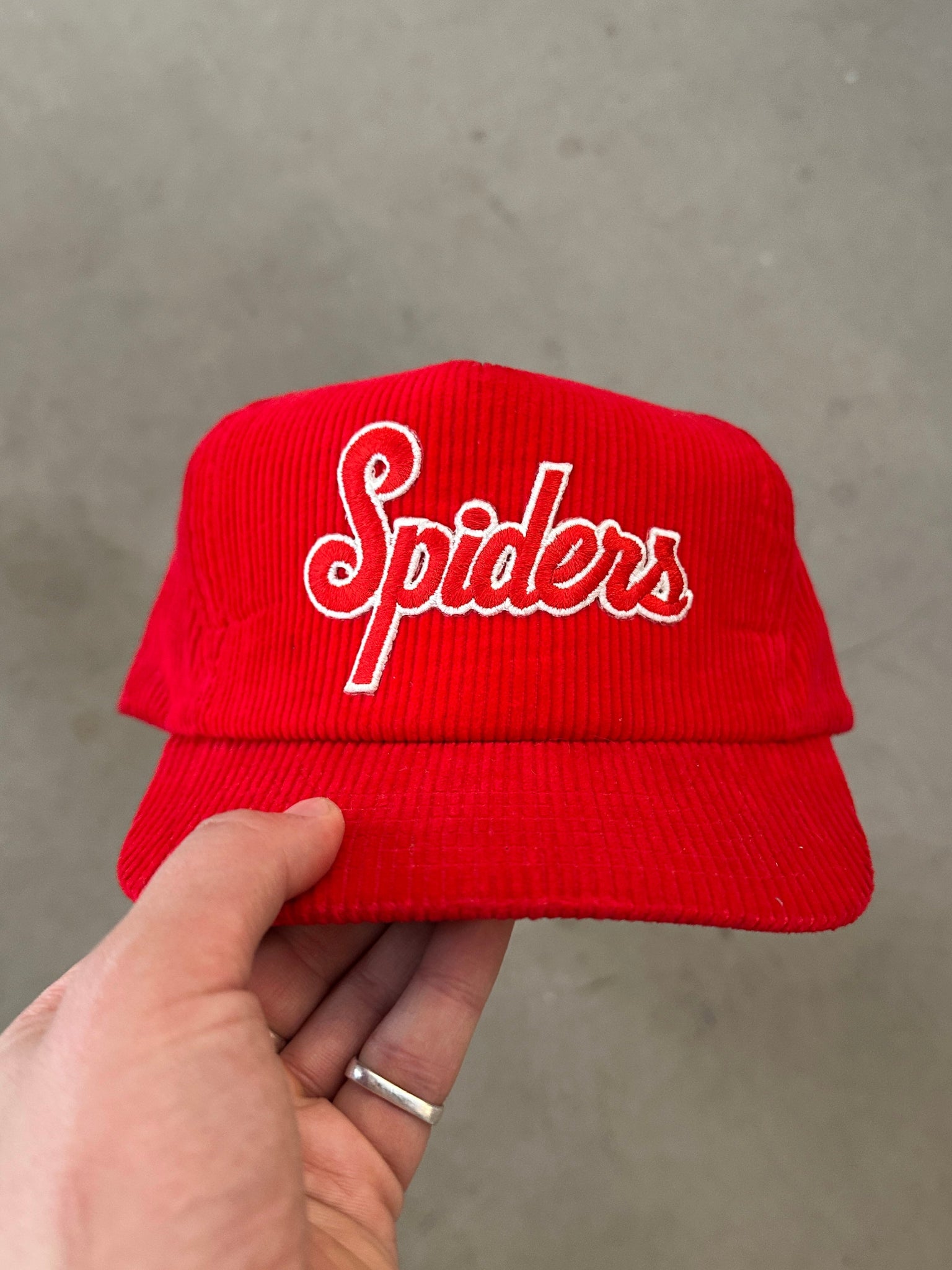 Red cap with 'Spiders' logo held by a hand against a neutral background