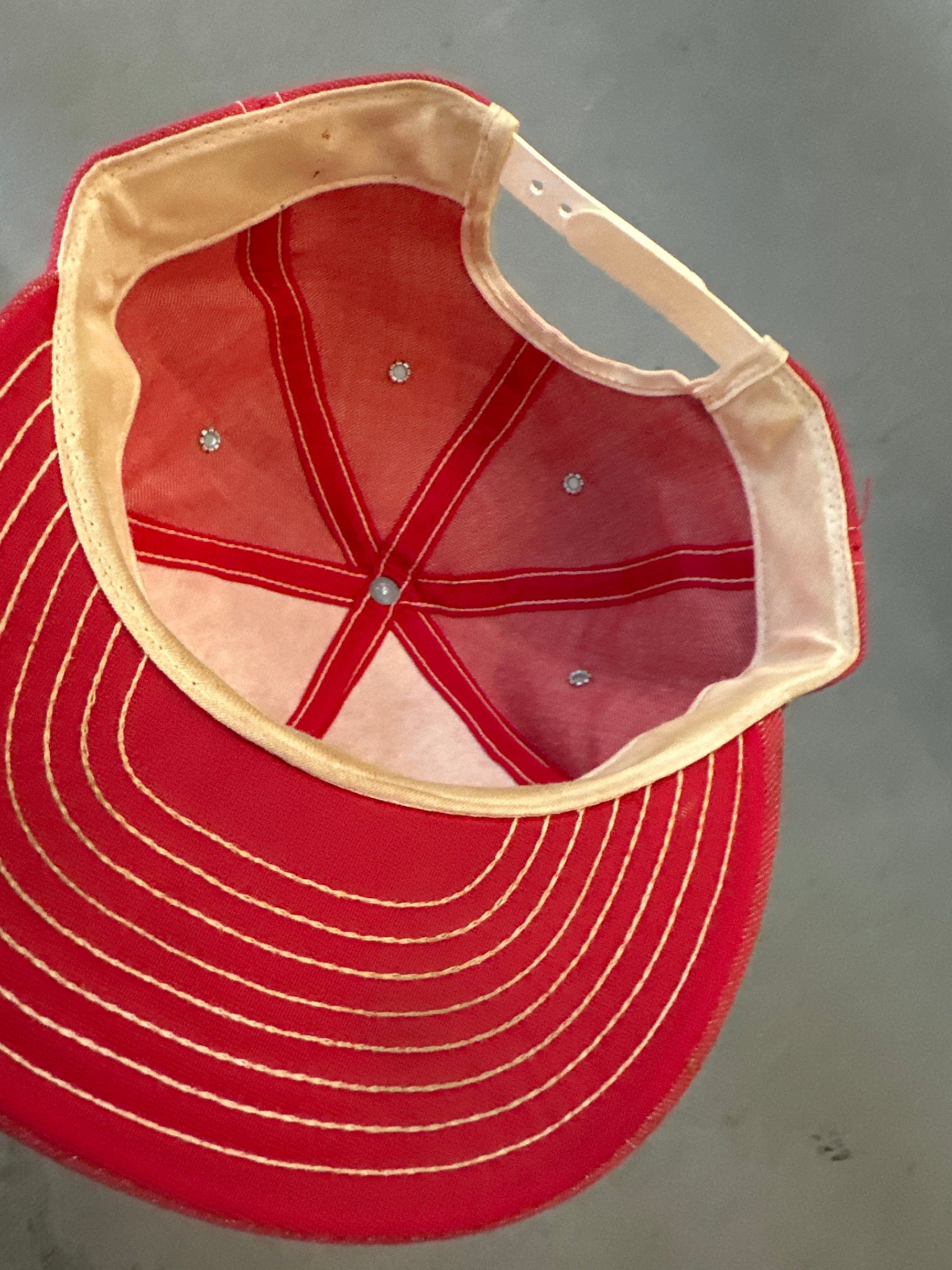 Red baseball cap with beige interior on a gray background