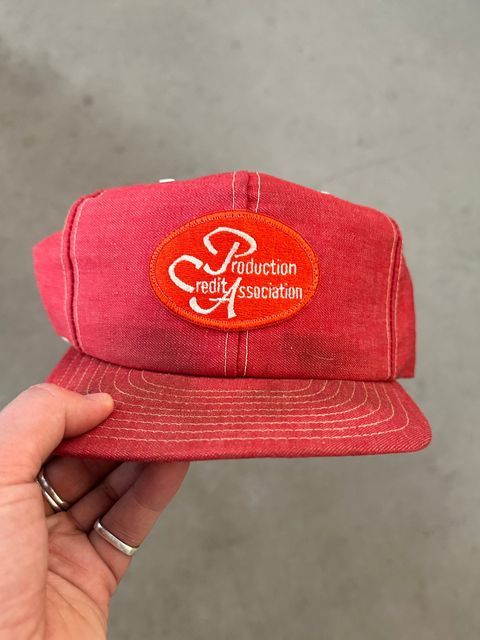 Red cap with a logo held by a hand against a gray background