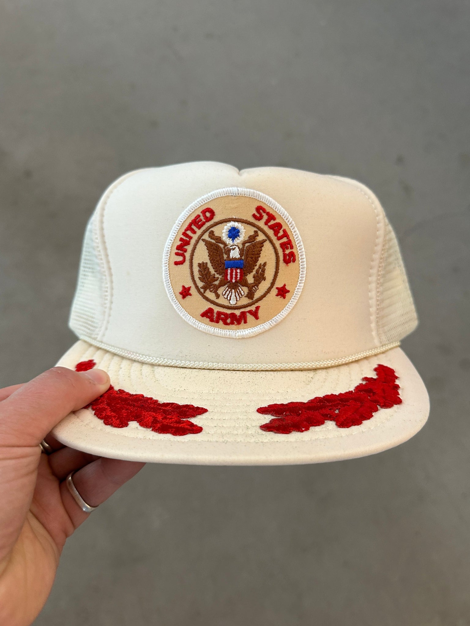 Beige cap with United States Army emblem held by a hand against a gray background