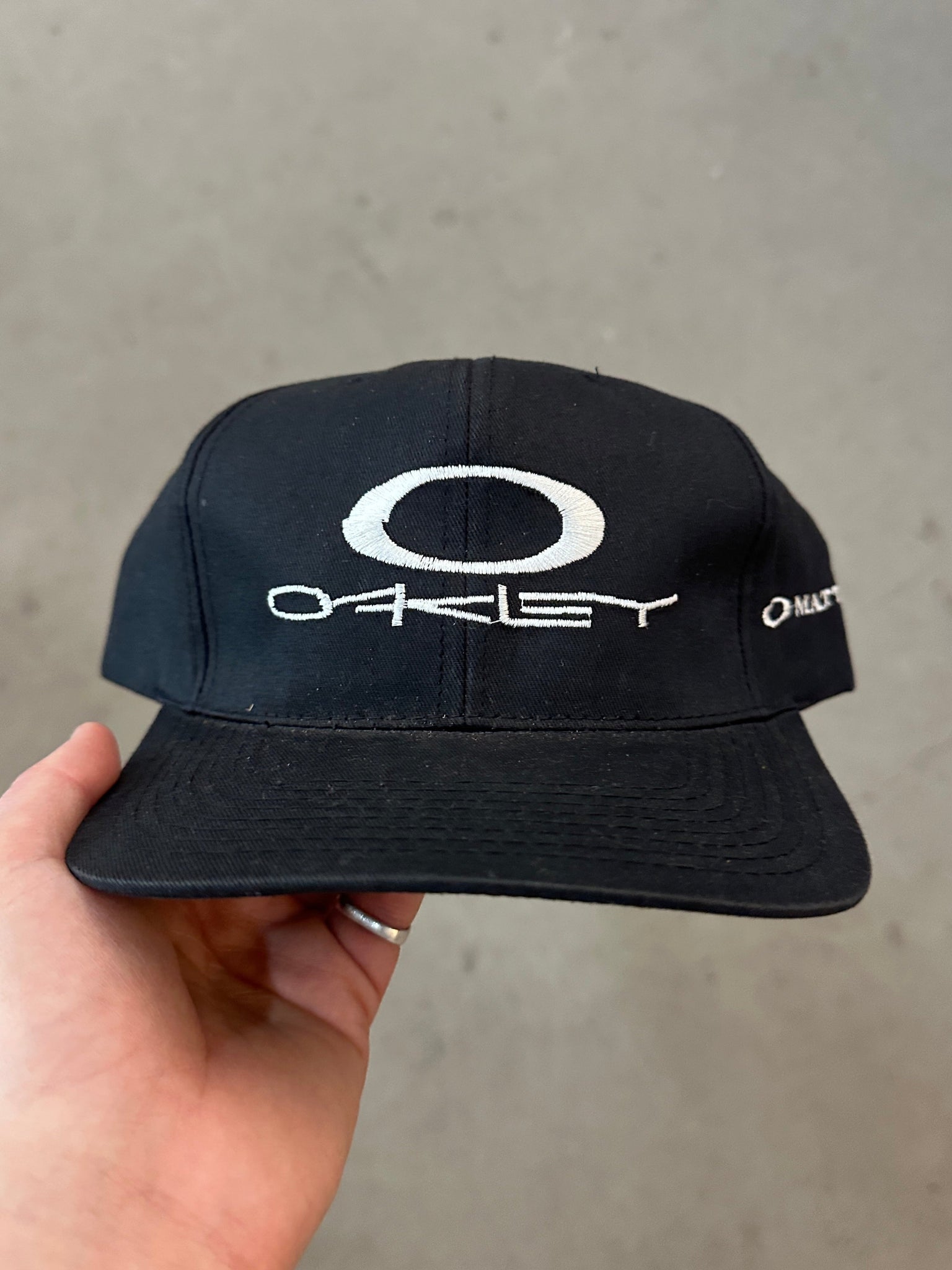 Black cap with Oakley logo held by a hand on a gray background
